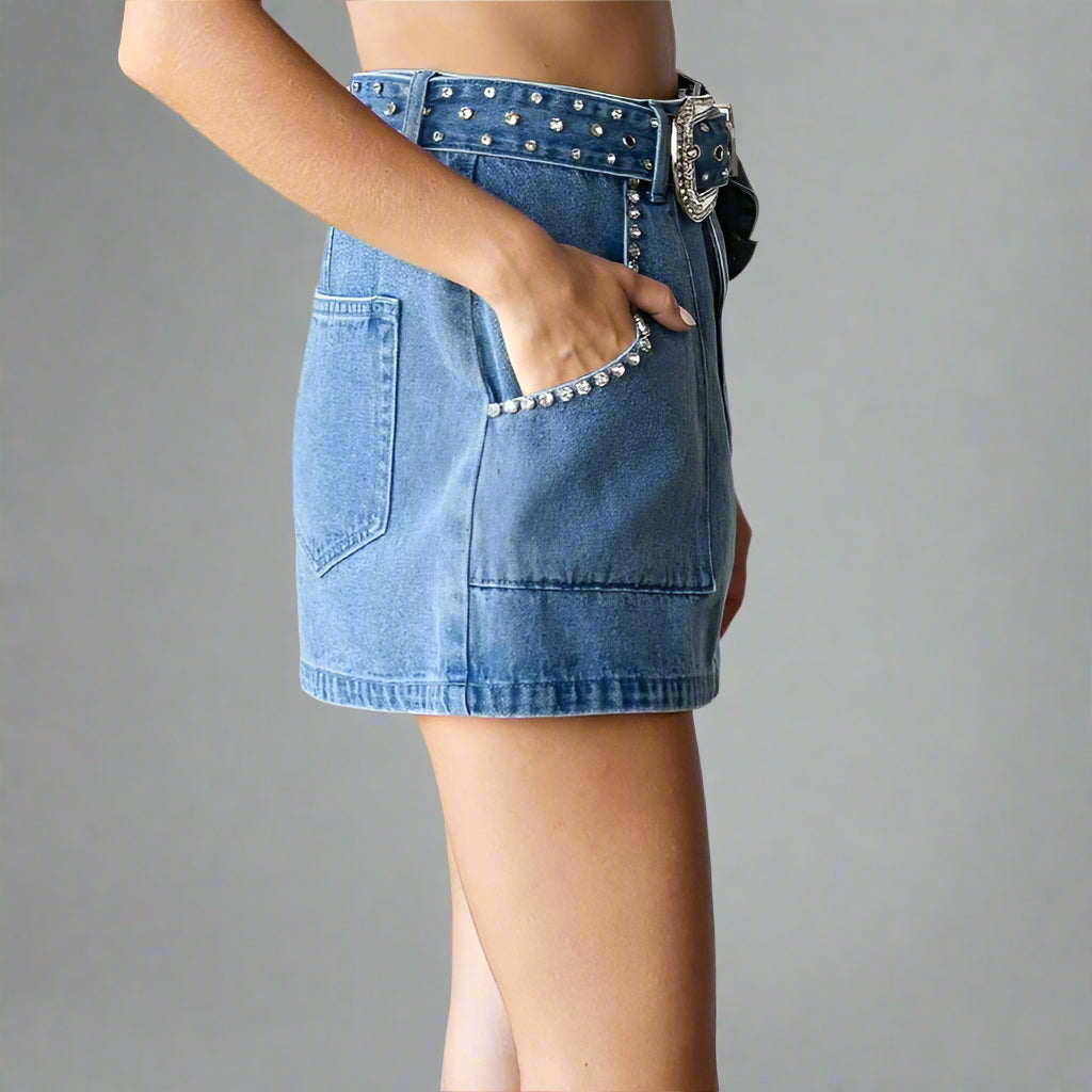 Person wearing a blue denim skirt with studded details in a minimal indoor setting.
